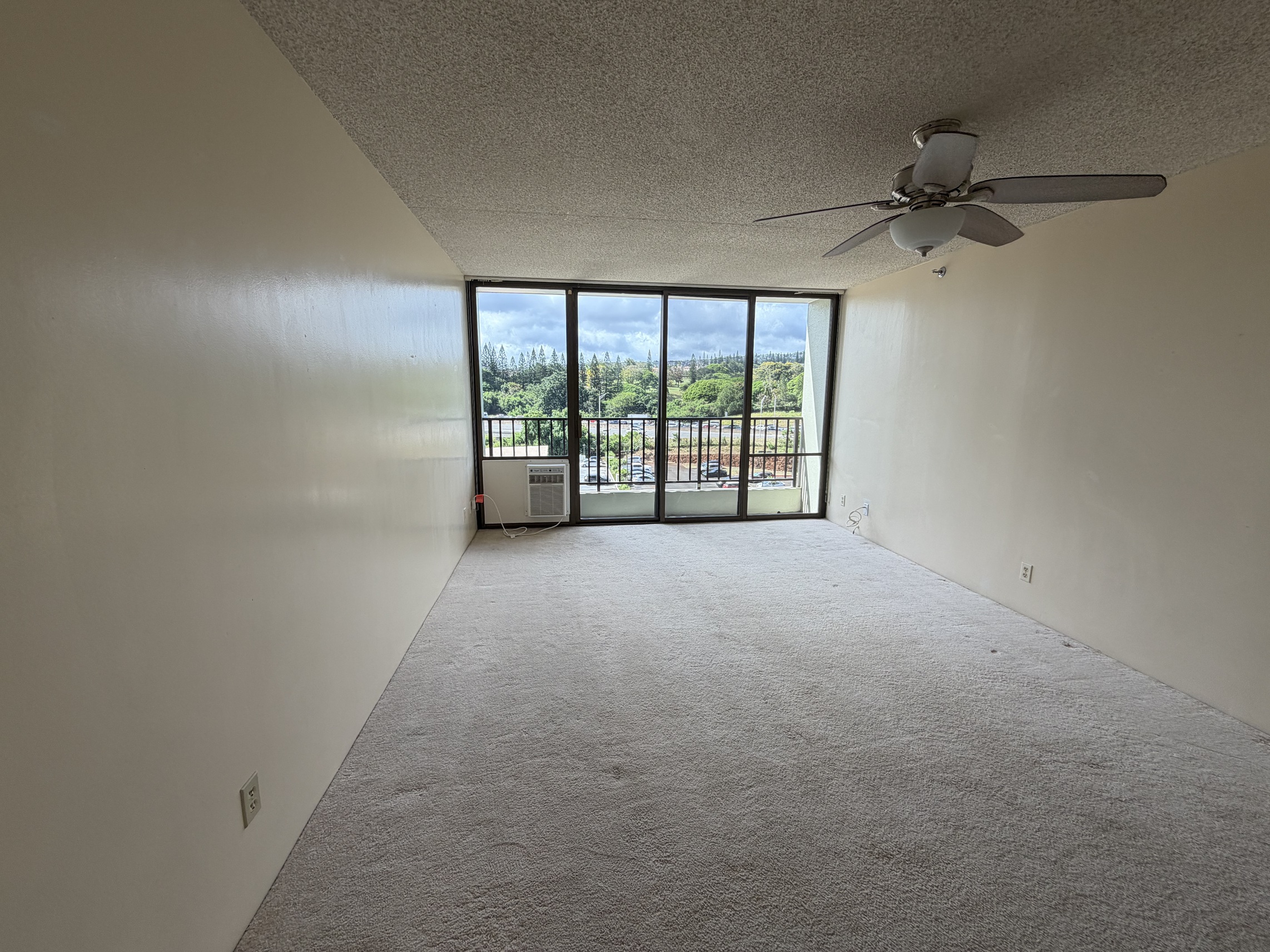 A room with a ceiling fan and a view of the outside through a sliding glass door.